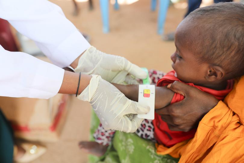 Halima’s son is having his upper arm circumference measured by the mobile health team