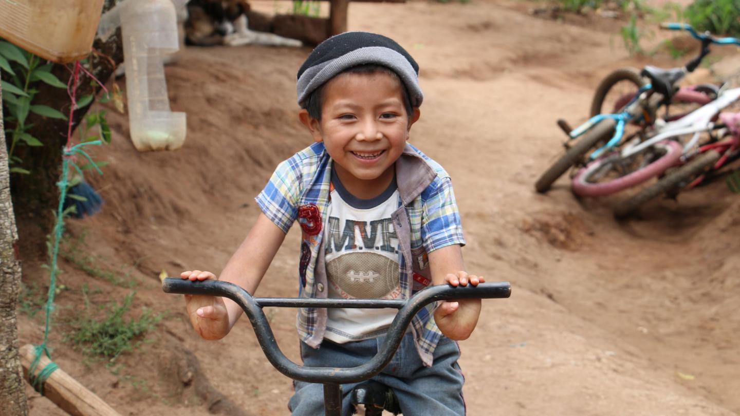 A Mayan child riding a bike outside his house