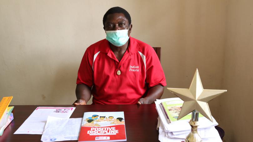 A head teacher (Mr Boniface) sitting behind his office desk