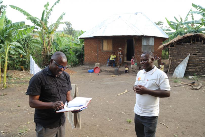 John (right) outside his new family home, with Save the Children staff member John Mateso (left)