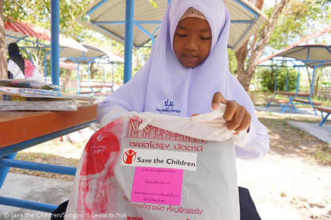 Sikin excitedly opens her distribution kits, including educational materials, school bags, and uniforms